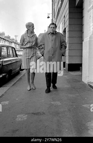 Actor Bill Wallis wearing a raincoat popularised by Premier Harold Wilson gets a light for his pipe from actress Myvanwyn Jenn . Bill and Myvanwyn will take the part of the Prime Minister and his wife in a play at the Theatre Royal in Stratford , London called Mrs Wilson's Diary . The theatre won a six month battle with the Lord Chamberlain's office to present the play . 18 September 1967 Stock Photo