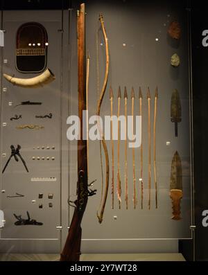 bows, spears, arrowheads, and a horn. Artifacts and weapons of early settlers displayed in a museum exhibit showcasing ancient survival tools. Stock Photo