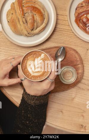 A woman holds coffee with her hands on a table in a coffee shop, surrounded by delicious pastries.Top view. Stock Photo