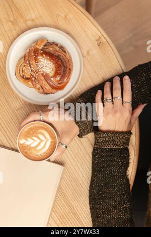 A woman holds coffee with her hands on a table in a coffee shop, surrounded by delicious pastries.Top view. Stock Photo