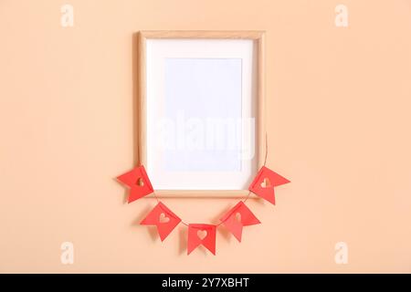Empty frame and bunting with hearts hanging on beige wall. Valentine's Day celebration Stock Photo