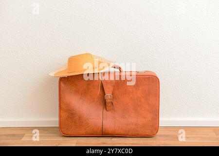 Brown retro leather suitcase with straw hat on floor in room Stock Photo