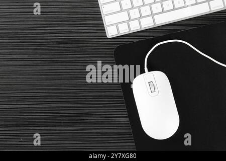 White computer mouse with mousepad and keyboard on black wooden table, flat lay Stock Photo