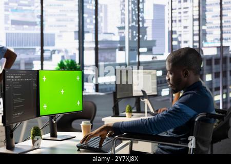Person with paraplegia testing and deploying programs and systems on green screen PC. Software engineer in wheelchair checking code on mockup PC, sitting at desk in office Stock Photo