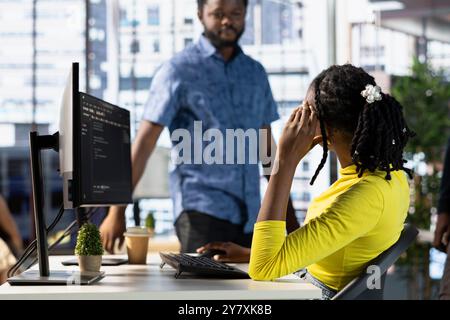 Programmer doing software debugging, asking for help from coworker, checking errors in lines of code. Employee fixing coding mistakes, being assisted by colleague sharing helpful advice Stock Photo