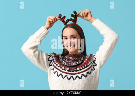 Young woman in sweater with Christmas reindeer horns on blue background Stock Photo