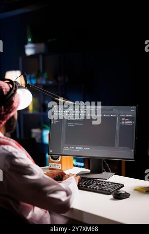 Traditional Middle Eastern developer compiles code on desktop computer, showcasing expertise in programming, algorithms, and software development. Selective focus on pc monitor displaying source code. Stock Photo