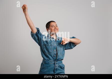 Happy young short hair woman in denim clothes dancing against grey background Stock Photo