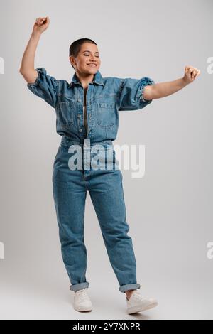 Full length of happy young short hair woman in denim clothes dancing against grey background Stock Photo