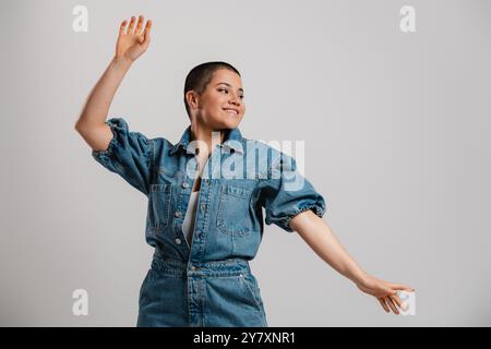 Joyful young short hair woman in denim clothes dancing and smiling against grey background Stock Photo