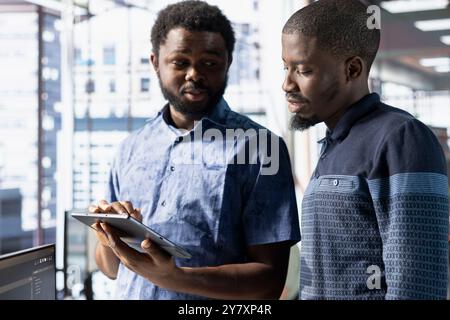 Coworkers looking at tablet, managing cloud computing resources and platforms to train machine learning models. Teamworking colleagues brainstorming while monitoring company systems Stock Photo
