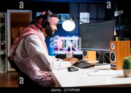 Middle Eastern software programmer typing code on a laptop showcasing the essence of software programming and development. Arab man with wireless headphones engrossed in running algorithms. Stock Photo