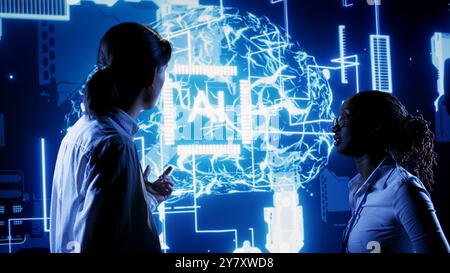 African american engineer and asian coworker looking at hologram of artificial intelligence human brain simulation. BIPOC IT team members interacting with AR AI visualization Stock Photo