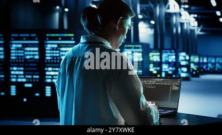 Experienced engineer running programming code on laptop, troubleshooting and updating data center equipment designed to accommodate server clusters, networking systems and storage arrays Stock Photo