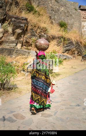 A village woman walking on a stone laid pathway with pot of water on her headb Stock Photo