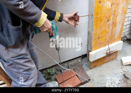 Worker is installing and assembling column formworks for concrete filling at building site. Wooden column formwork secured to masonry using studs. Con Stock Photo