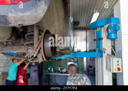 Mature experienced teacher standing underneath car on hydraulic ramp and teaching automotive trade to his students in the vocational school Stock Photo
