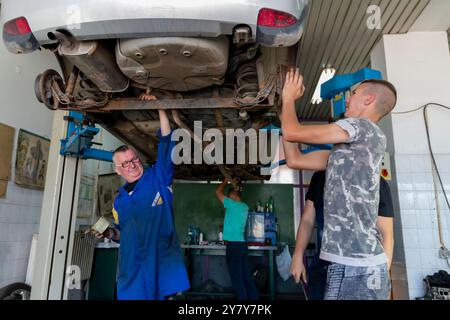 Mature experienced teacher standing underneath car on hydraulic ramp and teaching automotive trade to his students in the vocational school Stock Photo