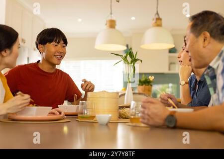 At home, asian family enjoying meal together, talking and smiling around dining table Stock Photo