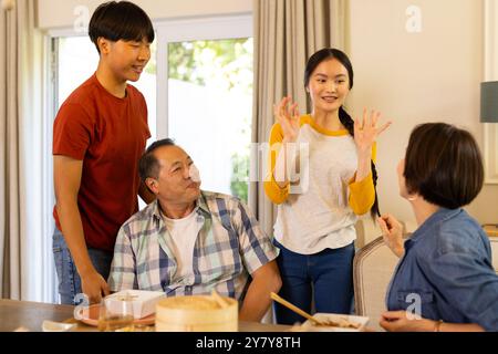 Smiling asian family enjoying meal together, engaging in lively conversation at home Stock Photo