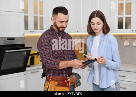 Woman and repairman signing documents near oven in kitchen Stock Photo