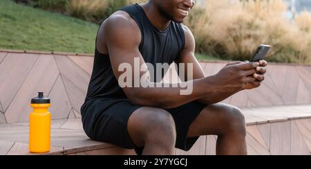 Close-up of happy African man in sportswear using smart phone while having a break after training Stock Photo