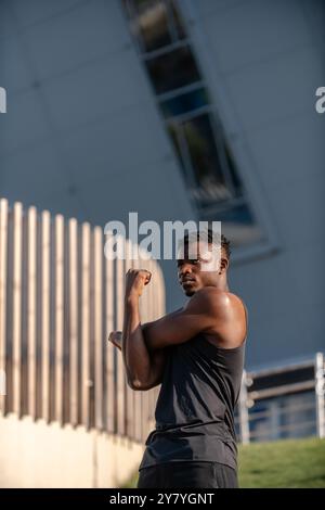 Concentrated young African man in sportswear doing stretching exercises while training outdoors Stock Photo