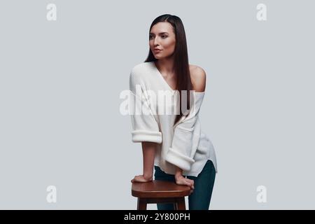 Simply stunning. Attractive young woman looking away and smiling while standing against grey background Stock Photo