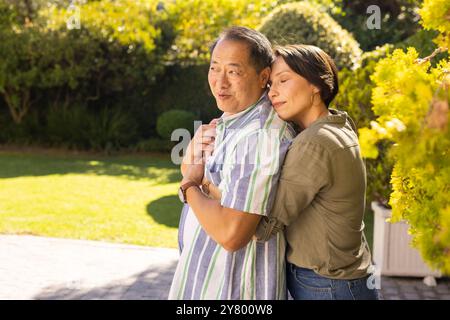 Hugging from behind, a couple, middle-aged woman showing affection to asian man in sunny garden Stock Photo