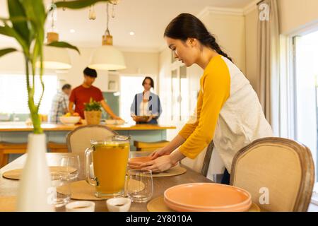 Setting table with plates and glasses, young asian woman preparing family meal in kitchen Stock Photo