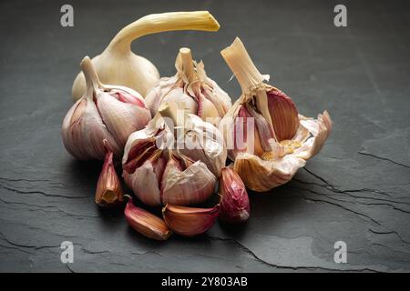 Whole garlic bulbs and garlic cloves lie on a black slate plate Stock Photo