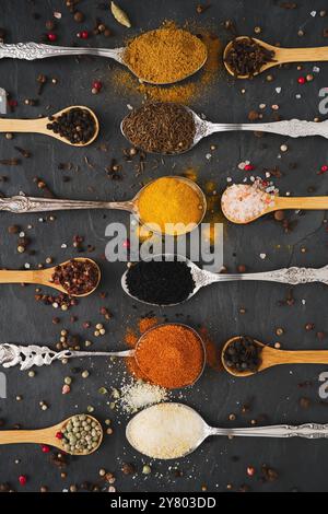 Many different exotic spices on tablespoons and small wooden spoons and vielen peppercorns arranged in a row in vertical portrait format on a large sl Stock Photo
