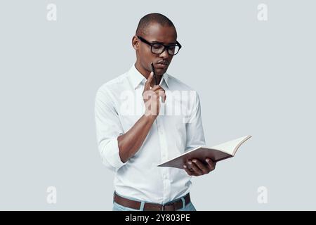Student. Handsome young African man reading something while standing against grey background Stock Photo