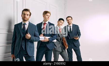 The team poses confidently against white studio background, each holding work-related materials, ready for their next business venture. Stock Photo