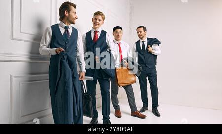 The team poses confidently against white studio background, each holding work-related materials, ready for their next business venture. Stock Photo