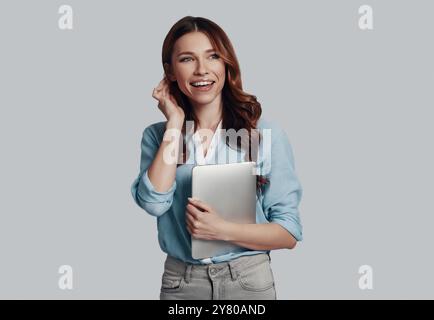 Full of fresh ideas. Attractive young woman looking away and smiling while standing against grey background Stock Photo