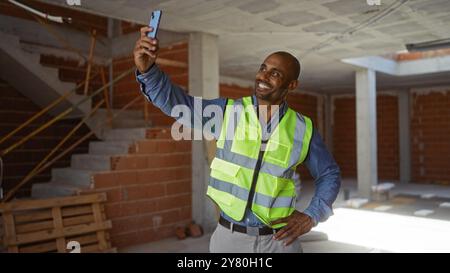 Young man taking selfie at construction site wearing safety vest and smiling during break Stock Photo