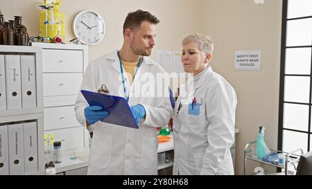 Man and woman scientists in lab coats discussing over clipboard in a well-equipped laboratory. Stock Photo