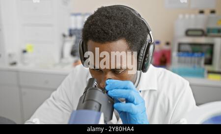 Focused african man wearing headphones analyzing samples under a microscope in a laboratory Stock Photo