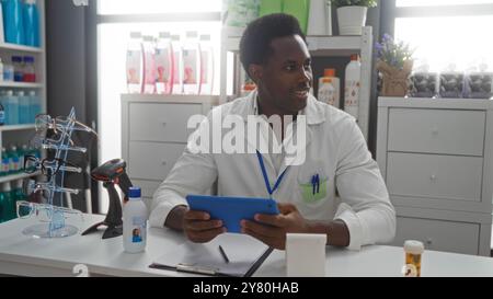 Young man sitting in a pharmacy store with a tablet, surrounded by various products and eyeglasses on display Stock Photo