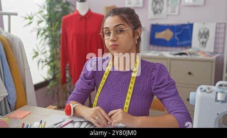 Young latina dressmaker with glasses in a tailor shop, focused on drafting patterns indoors. Stock Photo