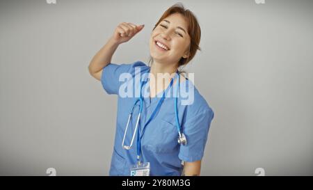 A cheerful young caucasian woman healthcare worker in blue scrubs posing joyfully against a white background. Stock Photo
