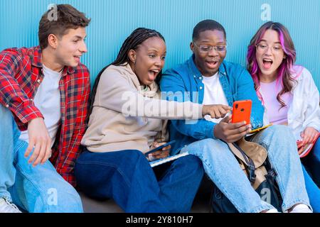 A group of diverse young people smiling sitting outdoors using smart phones Stock Photo