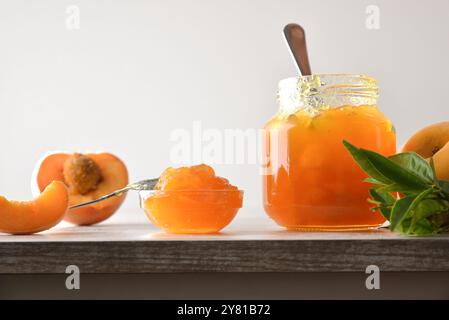 Jar and bowl with peach jam and fruit pieces and slices with leaves on wooden table white isolated background. Front view. Stock Photo