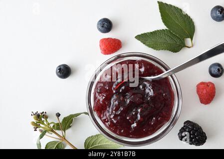 Detail of bowl with forest fruit jam isolated on white table with berries and leaves around. Top view. Stock Photo