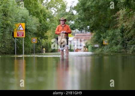 A man makes his way along a flooded road in Offord Cluny, Cambridgeshire. Further showery spells are expected across England, but drier, more settled weather conditions are set to arrive in the coming days. Picture date: Wednesday October 2, 2024. Stock Photo