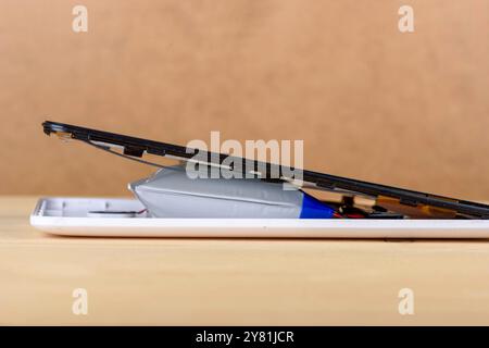 Disassembled smartphone with a swollen battery on a wooden surface against a beige background. Concept of battery damage and safety Stock Photo