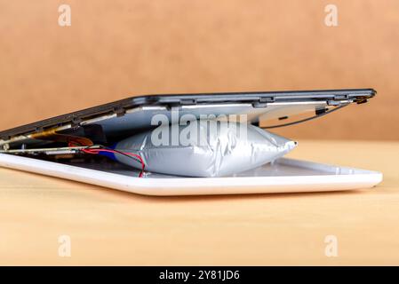 Close-up of a tablet with a swollen battery, showing internal damage on a wooden surface. Concept of electronic device hazard Stock Photo