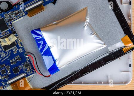 A swollen lithium-ion battery inside a disassembled electronic device on a desk. Concept of electronic repair and battery safety Stock Photo