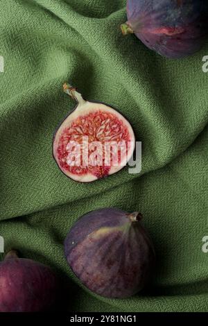 Fresh figs on a dark background, whole and sliced ripe, delicious and sweet figs with a kitchen knife on a green tablecloth, vertical top view Stock Photo